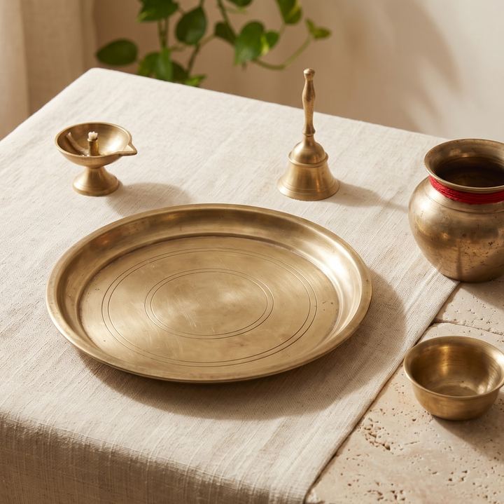 A brass thali, diya, bell, kalash and bowl on a cotton cloth.